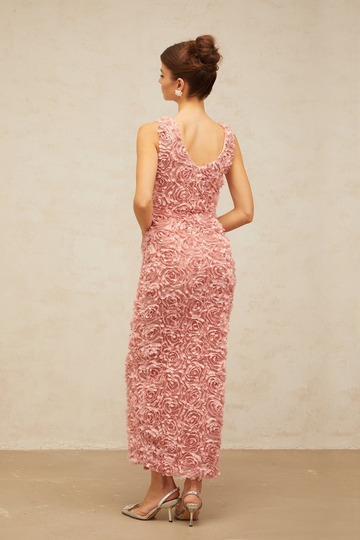 A woman wearing a long pink floral maxi dress with a V neckline and flowing skirt covered in faux flower patterns
