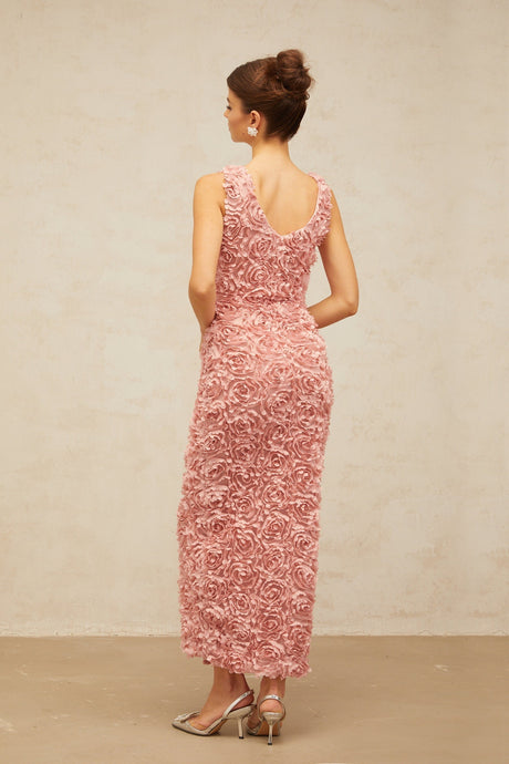 A woman wearing a long pink floral maxi dress with a V neckline and flowing skirt covered in faux flower patterns