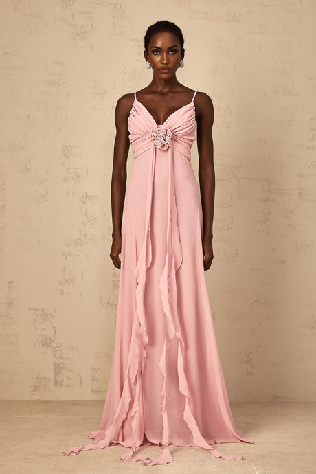 A woman wearing a long pink maxi dress with 3D petal details on the tulle fabric standing against a plain background