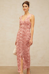 A woman wearing a long pink maxi dress with a Vneck and floral pattern standing in a relaxed pose against a plain background