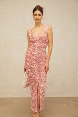 A woman wearing a long pink maxi dress with a Vneckline and floral pattern standing in a relaxed pose against a plain background