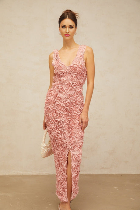 A woman wearing a long pink maxi dress with a Vneckline and floral pattern standing in a relaxed pose against a plain background