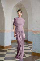 A woman wearing a long purple asymmetric dress with pleated details standing in a relaxed pose