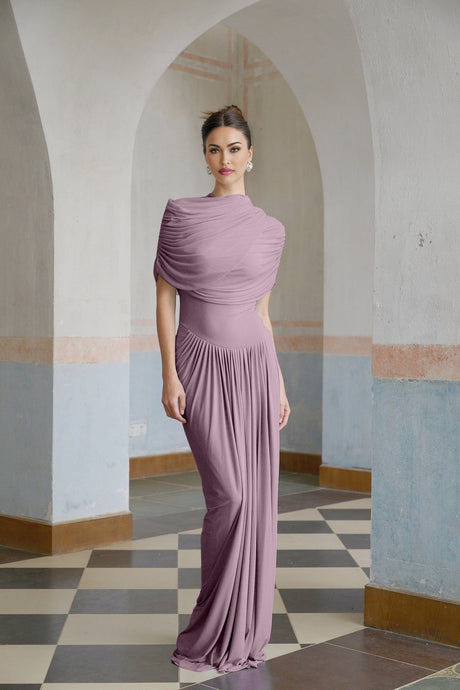 A woman wearing a long purple asymmetric dress with pleated details standing in a relaxed pose