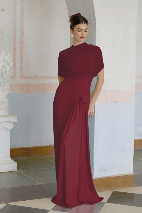 A woman wearing a long red asymmetric pleated maxi dress with one shoulder strap walking on a white background