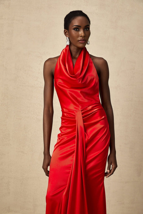 A woman wearing a long red satin dress with a halter neckline and draped fabric detail