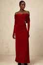 A woman wearing a long red velvet dress with ruched detailing and a fitted silhouette standing against a plain background