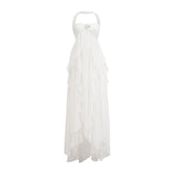 A woman wearing a long white chiffon maxi dress with ruffles and a halter neckline