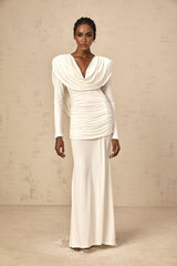 A woman wearing a long white fitted dress with ruched detailing standing in a relaxed pose