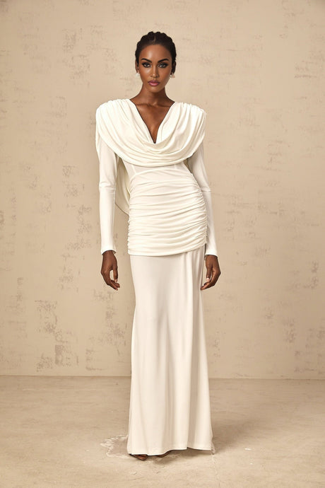 A woman wearing a long white fitted dress with ruched detailing standing in a relaxed pose