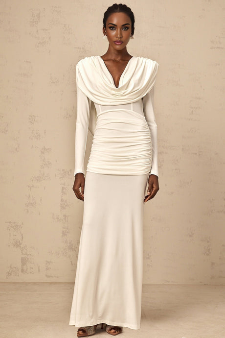 A woman wearing a long white fitted maxi dress with ruched detailing standing against a plain background