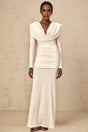 A woman wearing a long white fitted maxi dress with ruched detailing standing against a plain background