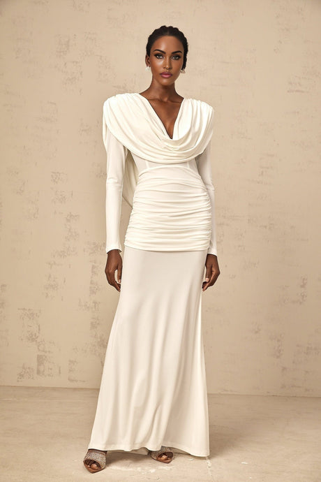 A woman wearing a long white fitted maxi dress with ruched detailing standing in a relaxed pose
