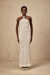 A woman wearing a long white halterneck maxi dress with embellishments standing against a plain background