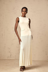 A woman wearing a long white knitted maxi dress with faux pearl embellishments standing in a neutral background
