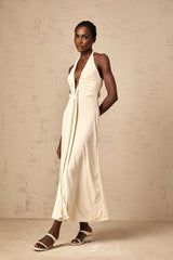 A woman wearing a long white maxi dress with a deep V neckline and draped fabric detail