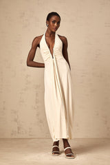 A woman wearing a long white maxi dress with a deep V neckline and draped fabric details