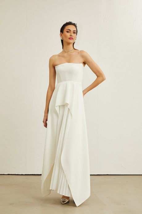 A woman wearing a long white pleated maxi dress with an offshoulder neckline