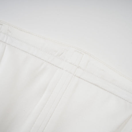 A woman wearing a long white pleated maxi dress with an offshoulder neckline