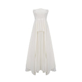 A woman wearing a long white pleated maxi dress with an offshoulder neckline