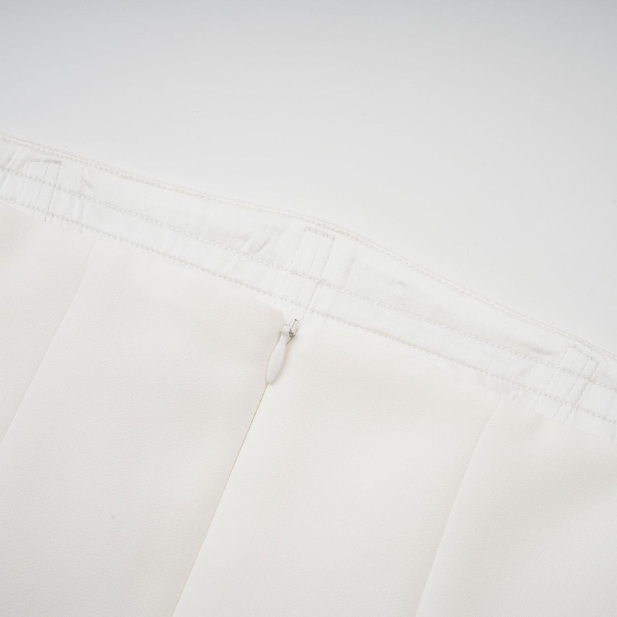 A woman wearing a long white pleated maxi dress with an offshoulder neckline