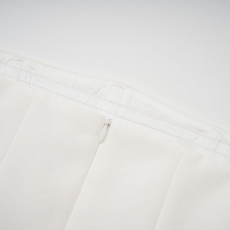A woman wearing a long white pleated maxi dress with an offshoulder neckline