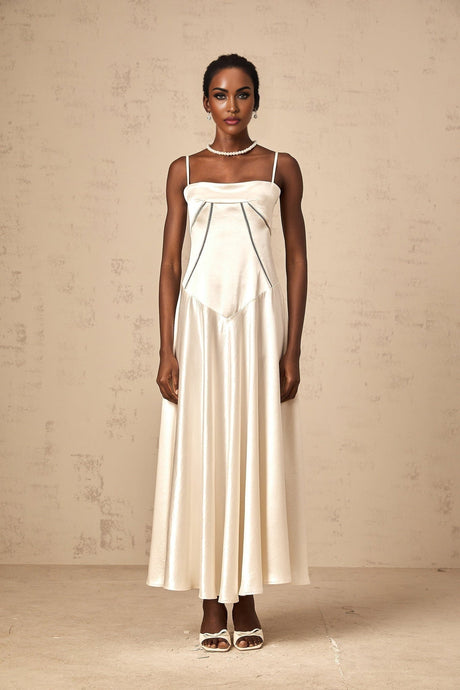 A woman wearing a long white satin dress with a flared skirt standing against a plain background