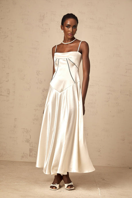 A woman wearing a long white satin dress with a flared skirt standing against a plain background