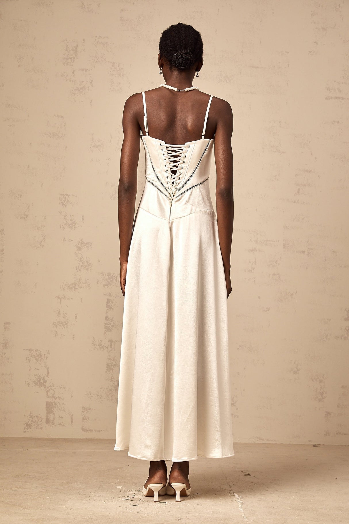 A woman wearing a long white satin maxi dress with a flared skirt and fitted bodice standing in a relaxed pose