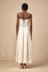 A woman wearing a long white satin maxi dress with a flared skirt and fitted bodice standing in a relaxed pose