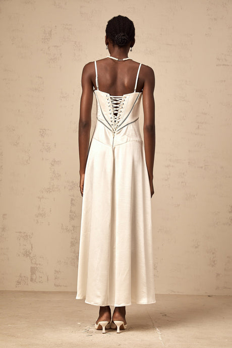 A woman wearing a long white satin maxi dress with a flared skirt and fitted bodice standing in a relaxed pose