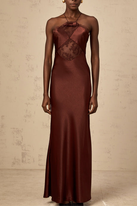 A woman wearing a long winered maxi dress with lace panels and satin fabric standing elegantly against a plain background