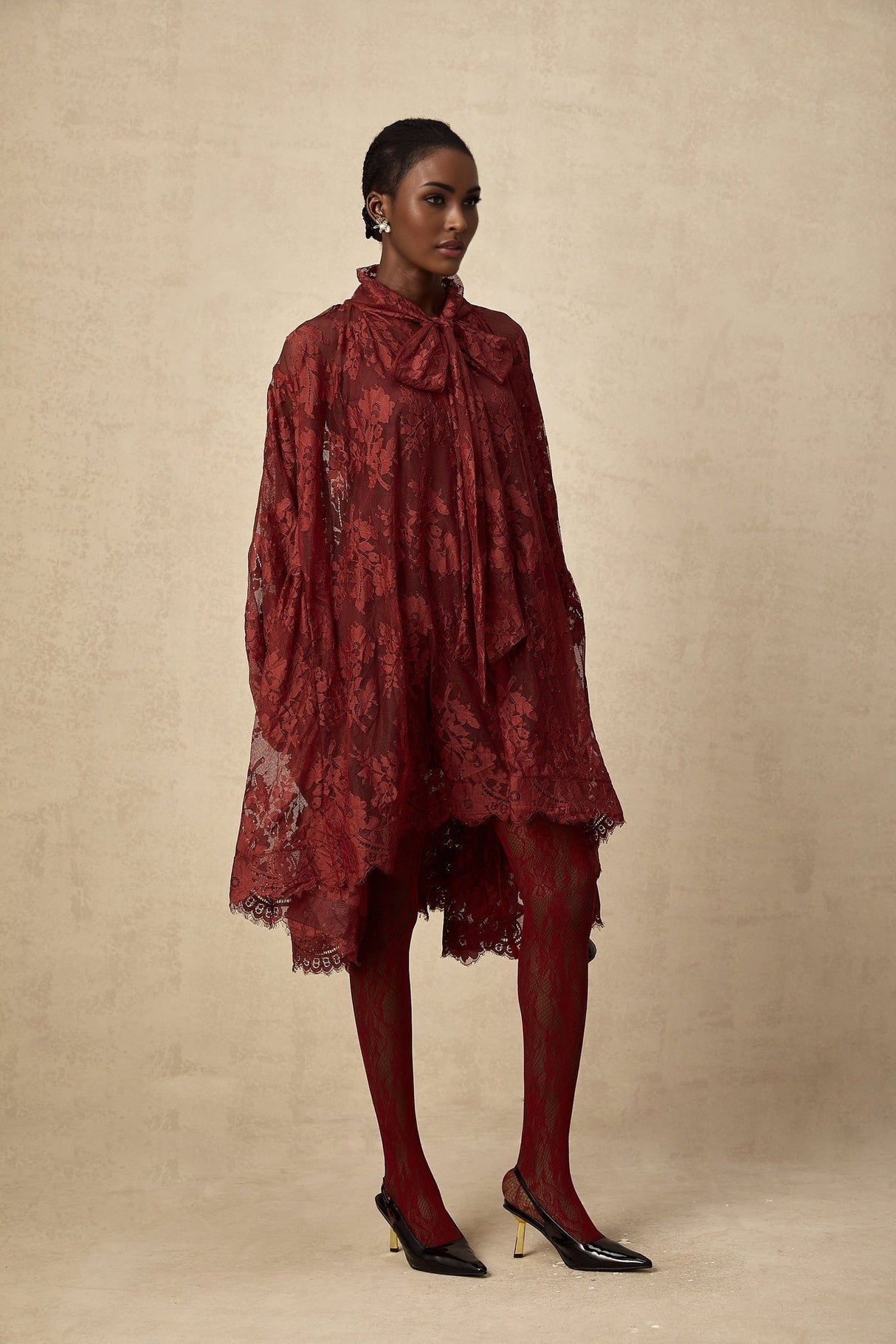 A woman wearing a loose fitting red dress made of delicate chantilly lace standing in a relaxed pose