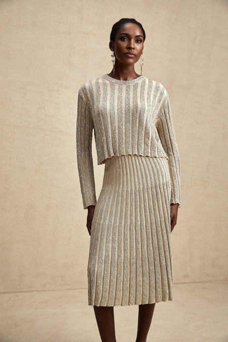 A woman wearing a matching champagne colored knit top and skirt set with subtle horizontal stripes standing against a plain background