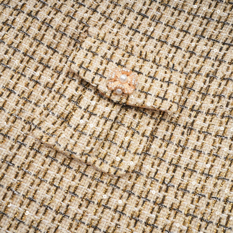 A woman wearing a matching gold tweed jacket and skirt set with sequin embellishments The jacket has long sleeves and the skirt is knee length Both pieces shimmer in the light
