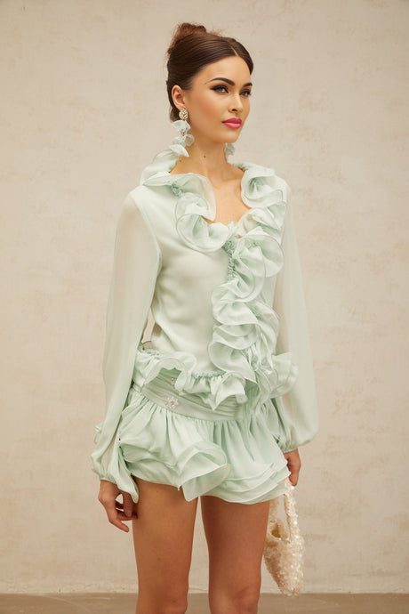 A woman wearing a matching green chiffon outfit consisting of a flounced blouse and skirt set by Noémie