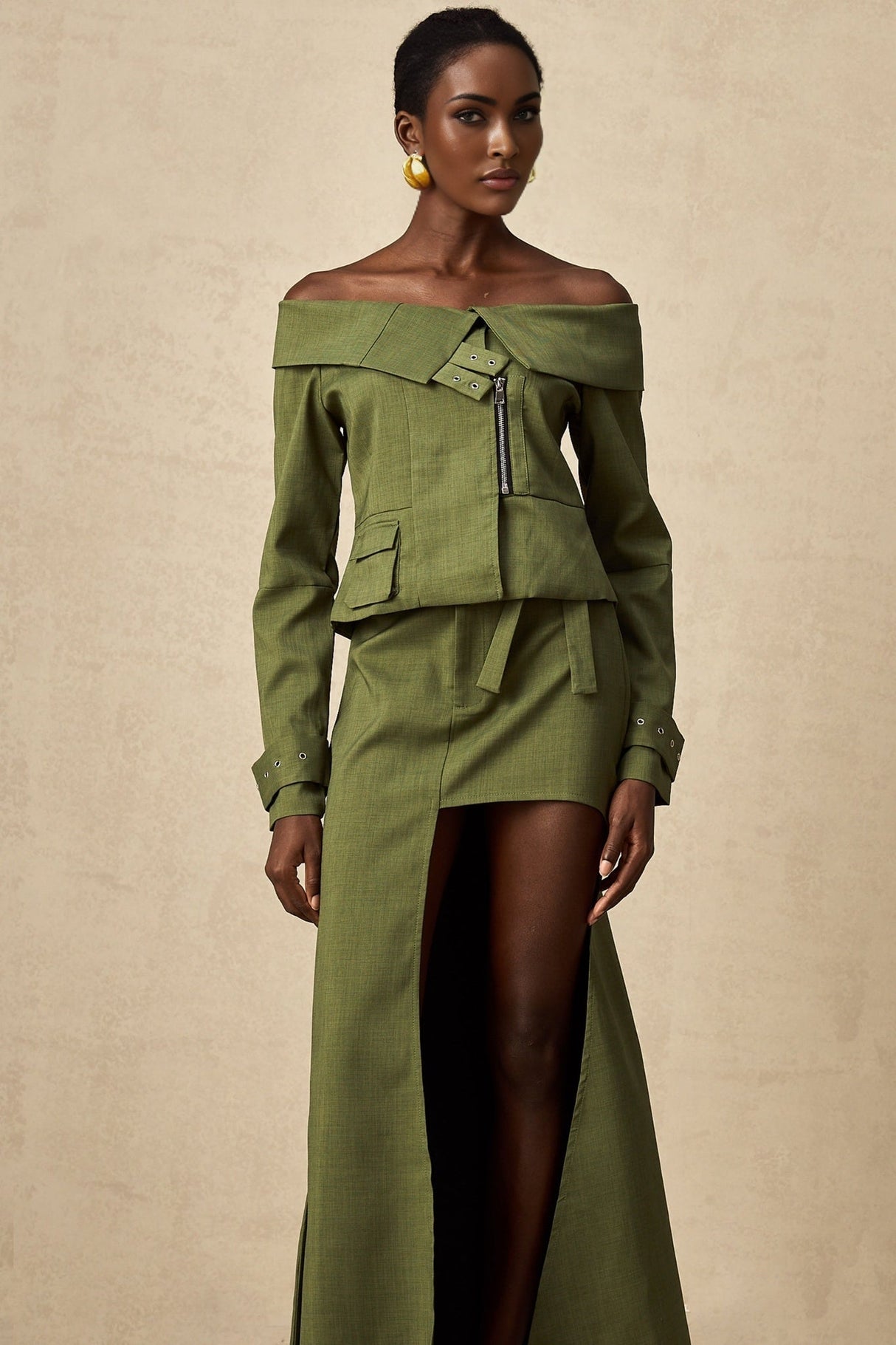 A woman wearing a matching green outfit consisting of an asymmetric jacket and skirt set designed by Éléna