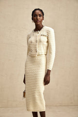 A woman wearing a matching knit cardigan and skirt set with embellishments The cardigan has long sleeves and the skirt falls to knee length Both pieces feature decorative details and are in a coordinating color