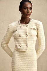 A woman wearing a matching knit cardigan and skirt set with embellishments The cardigan has long sleeves and the skirt falls to mid thigh Both pieces feature a light colored knit fabric with decorative details