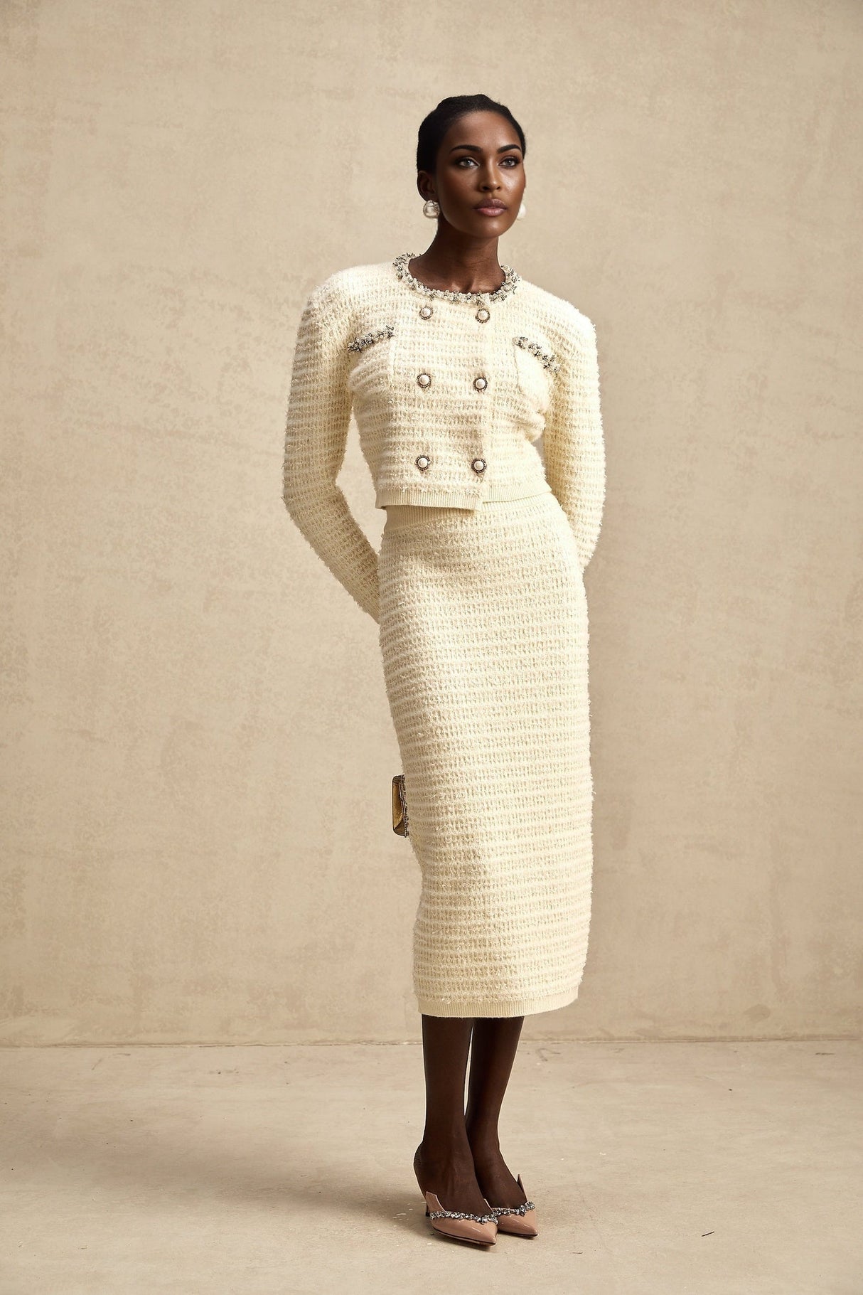 A woman wearing a matching knit cardigan and skirt set with embellishments The cardigan is open in the front and the skirt falls to about knee length The set is likely in a light color with decorative details
