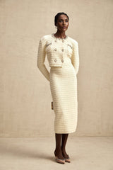 A woman wearing a matching knit cardigan and skirt set with embellishments The cardigan is open in the front and the skirt falls to about knee length The set is likely in a light color with decorative details