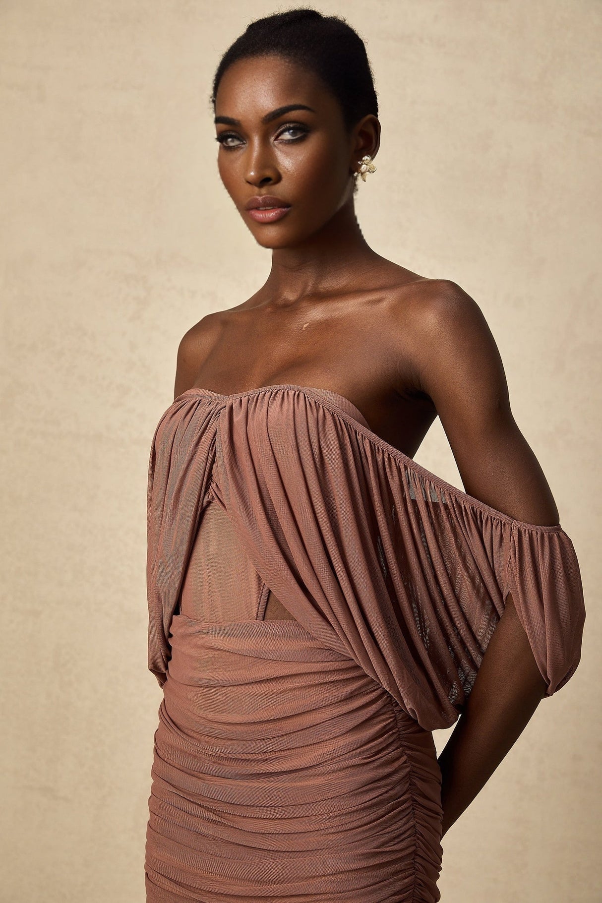 A woman wearing a matching offshoulder bodysuit and skirt set in a light color standing against a plain background