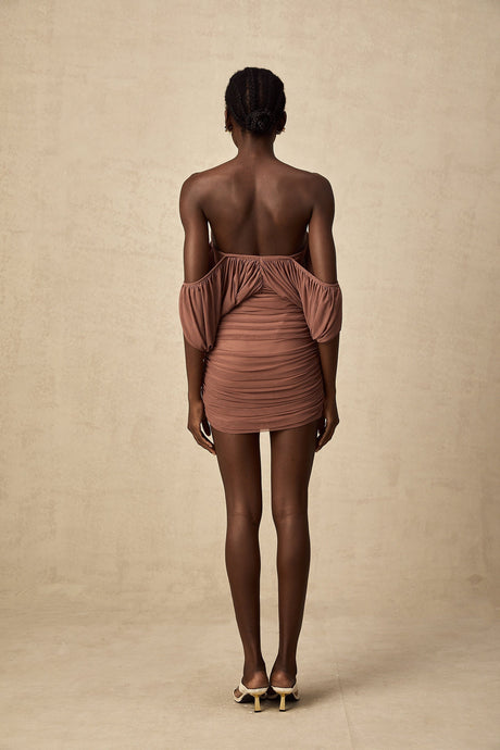 A woman wearing a matching offshoulder bodysuit and skirt set in a light color standing against a plain background
