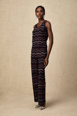 A woman wearing a matching set consisting of a crochet knit top and trousers with a zigzag pattern in a light color The top has short sleeves and the trousers are wide legged