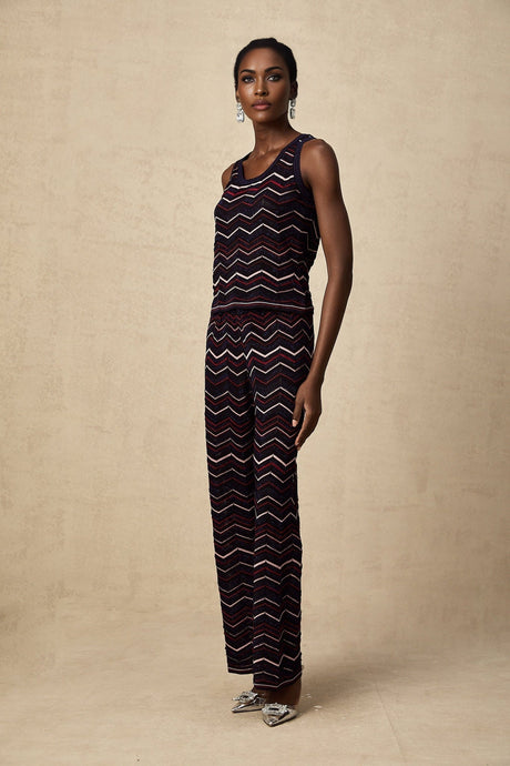 A woman wearing a matching set consisting of a crochet knit top and trousers with a zigzag pattern in a light color The top has short sleeves and the trousers are wide legged