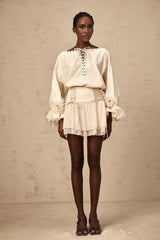 A woman wearing a matching set consisting of a light colored ruffled blouse with self tie details and a coordinating skirt