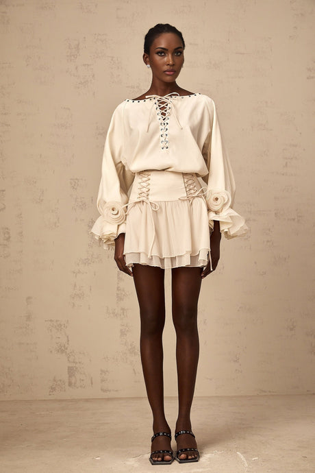 A woman wearing a matching set consisting of a light colored ruffled blouse with self tie details and a coordinating skirt
