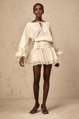 A woman wearing a matching set consisting of a ruffled blouse with selftie details and a coordinating skirt in a light colored fabric