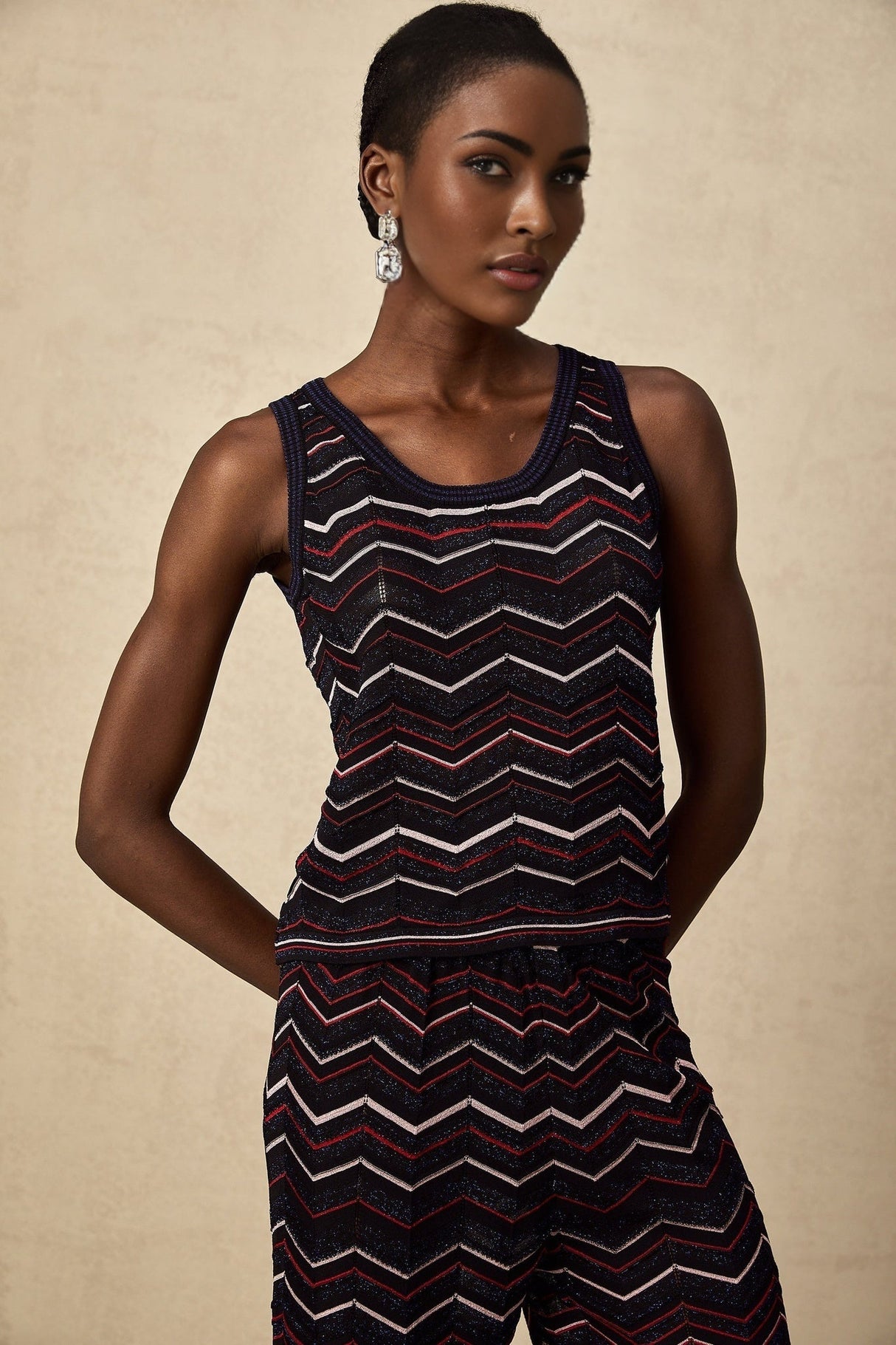 A woman wearing a matching set consisting of a zigzag patterned crochet knit top and trousers in a light color The top has short sleeves and the trousers are wide legged The set has a bohemian summer style