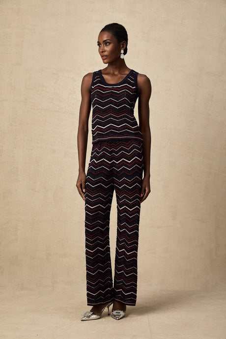 A woman wearing a matching set consisting of a zigzag patterned crochet knit top and trousers in a light color The top is sleeveless with a scoop neck and the trousers are wide leg The set has a bohemian summer look